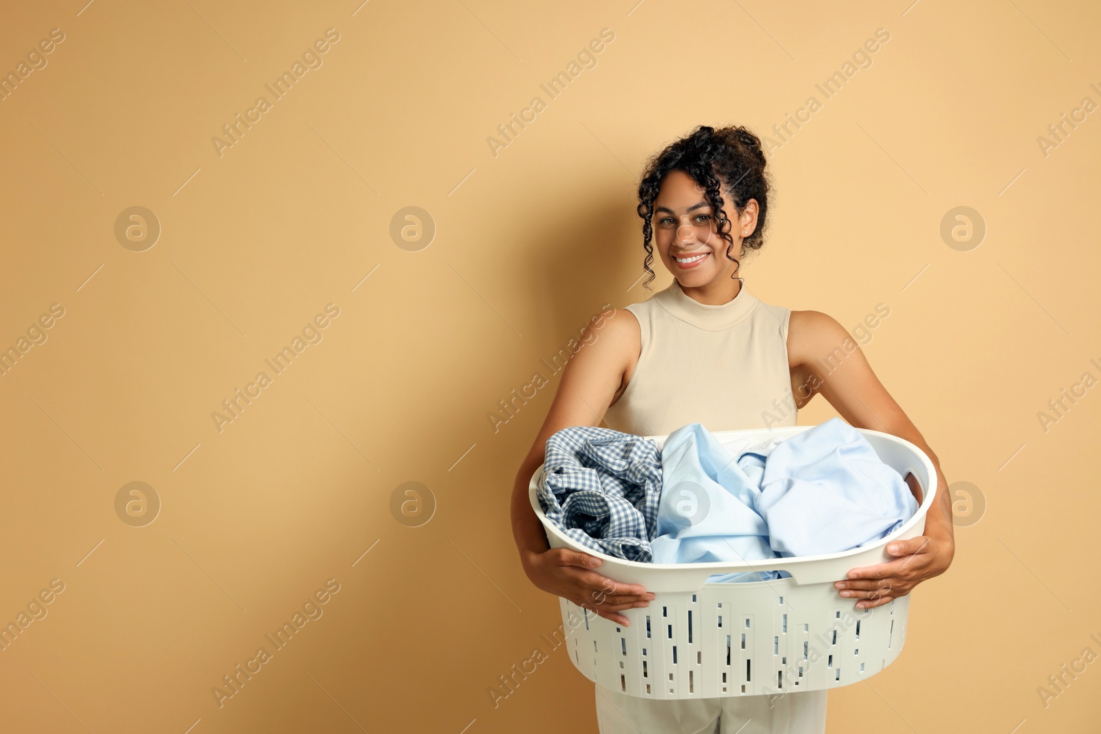 Photo of Happy woman with basket full of laundry on beige background, space for text