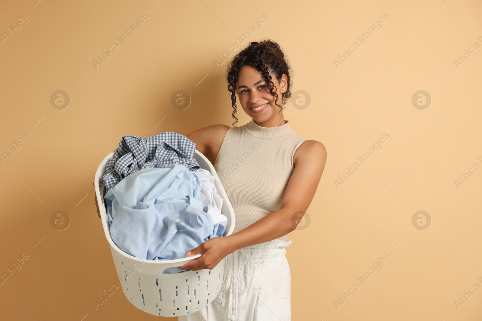 Photo of Happy woman with basket full of laundry on beige background