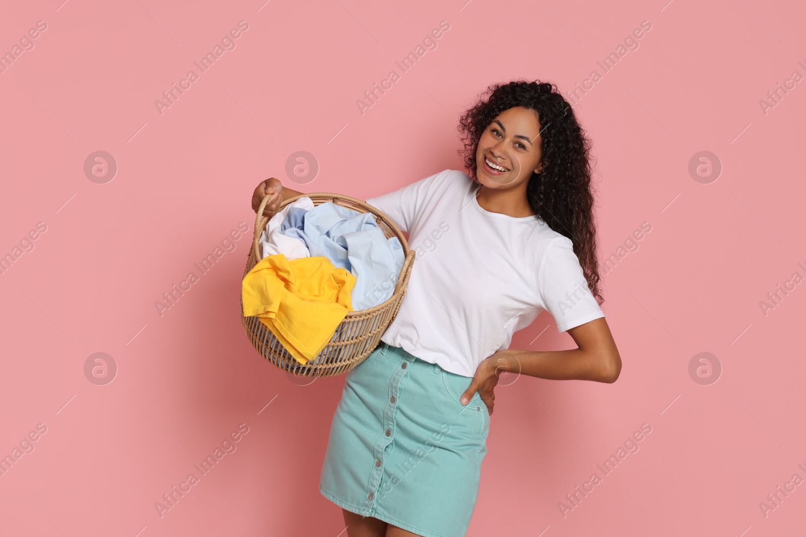 Photo of Happy woman with basket full of laundry on pink background