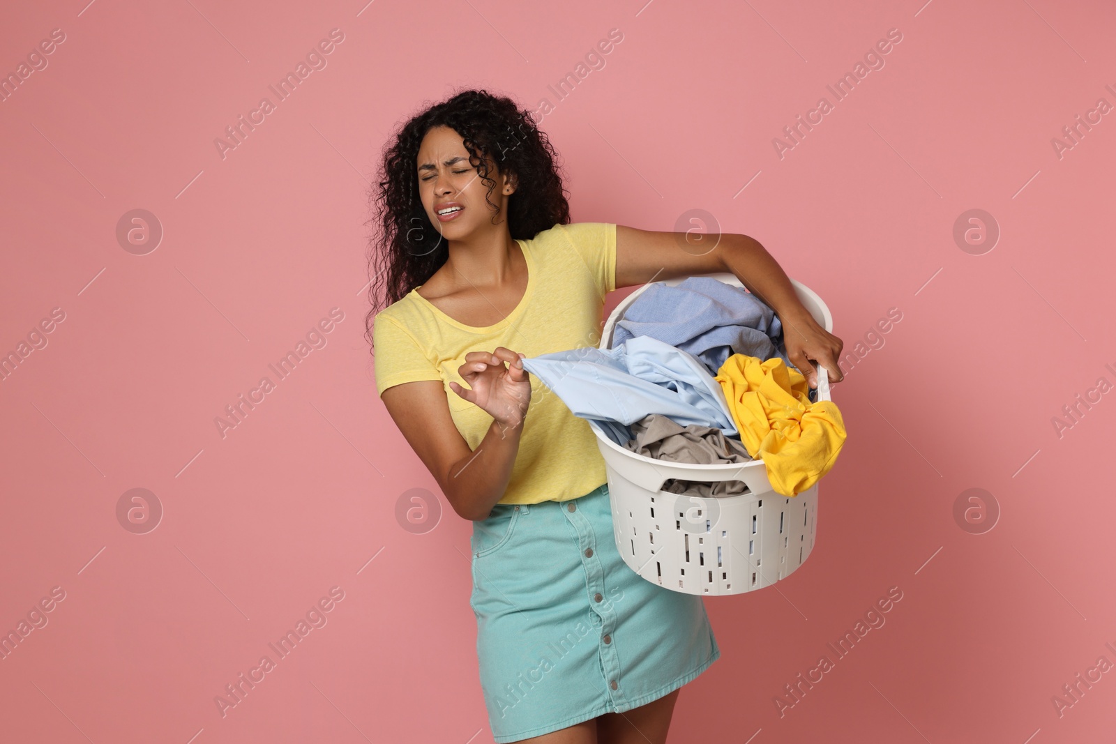 Photo of Displeased woman with basket full of laundry on pink background