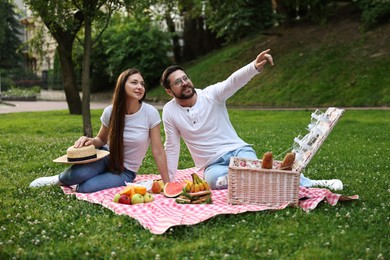 Photo of Romantic picnic. Smiling man pointing at something to his girlfriend on green grass outdoors