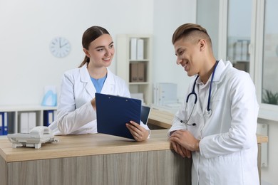 Professional receptionist and doctor at wooden desk in hospital