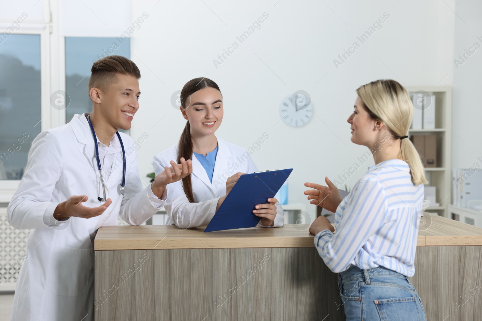 Photo of Professional receptionist and doctor working with patient at wooden desk in hospital