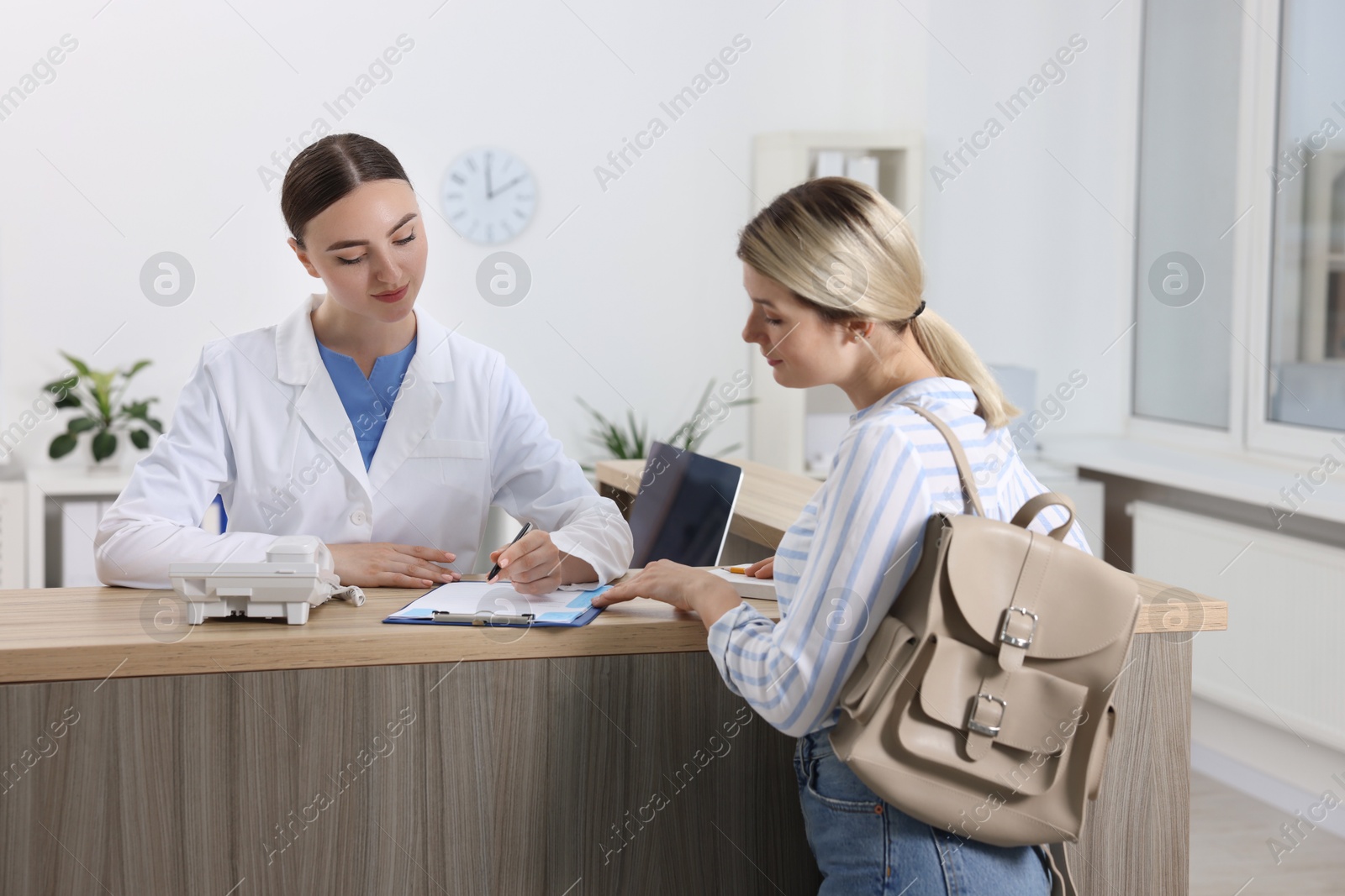 Photo of Professional receptionist working with patient at wooden desk in hospital