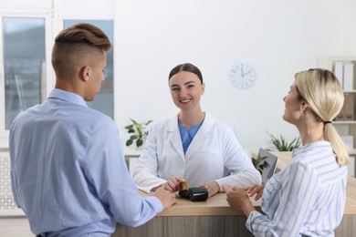 Receptionist taking payment from client via terminal at hospital