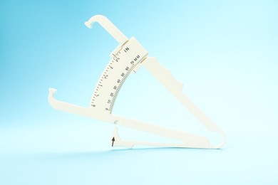 Photo of Plastic body fat caliper on light blue background