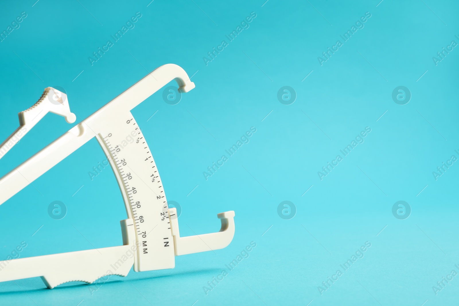 Photo of Plastic body fat caliper on light blue background, closeup. Space for text