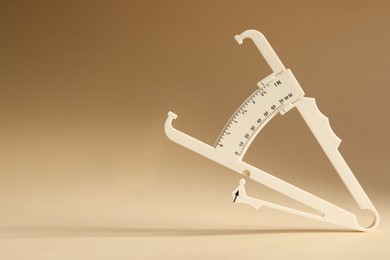 Plastic body fat caliper on beige background. Space for text