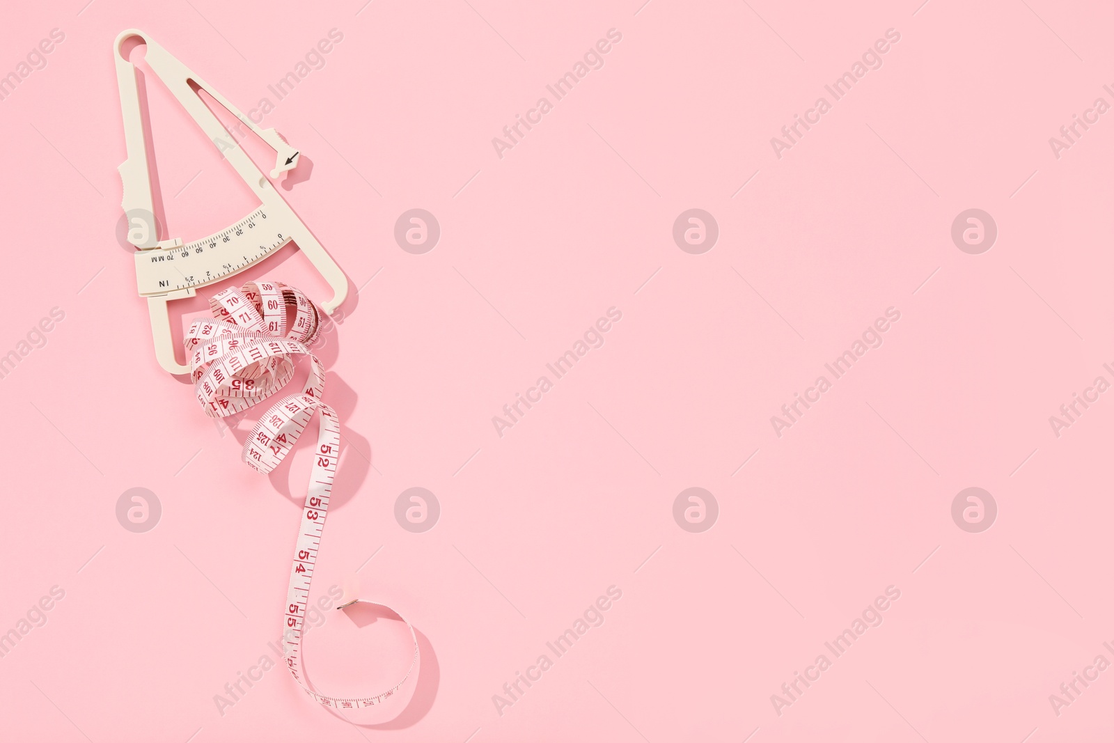 Photo of Body fat caliper and measuring tape on pink background, top view. Space for text