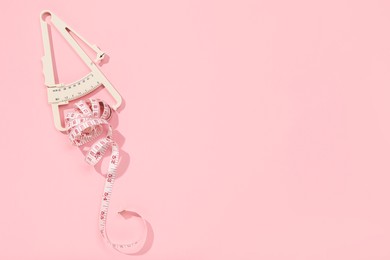 Photo of Body fat caliper and measuring tape on pink background, top view. Space for text