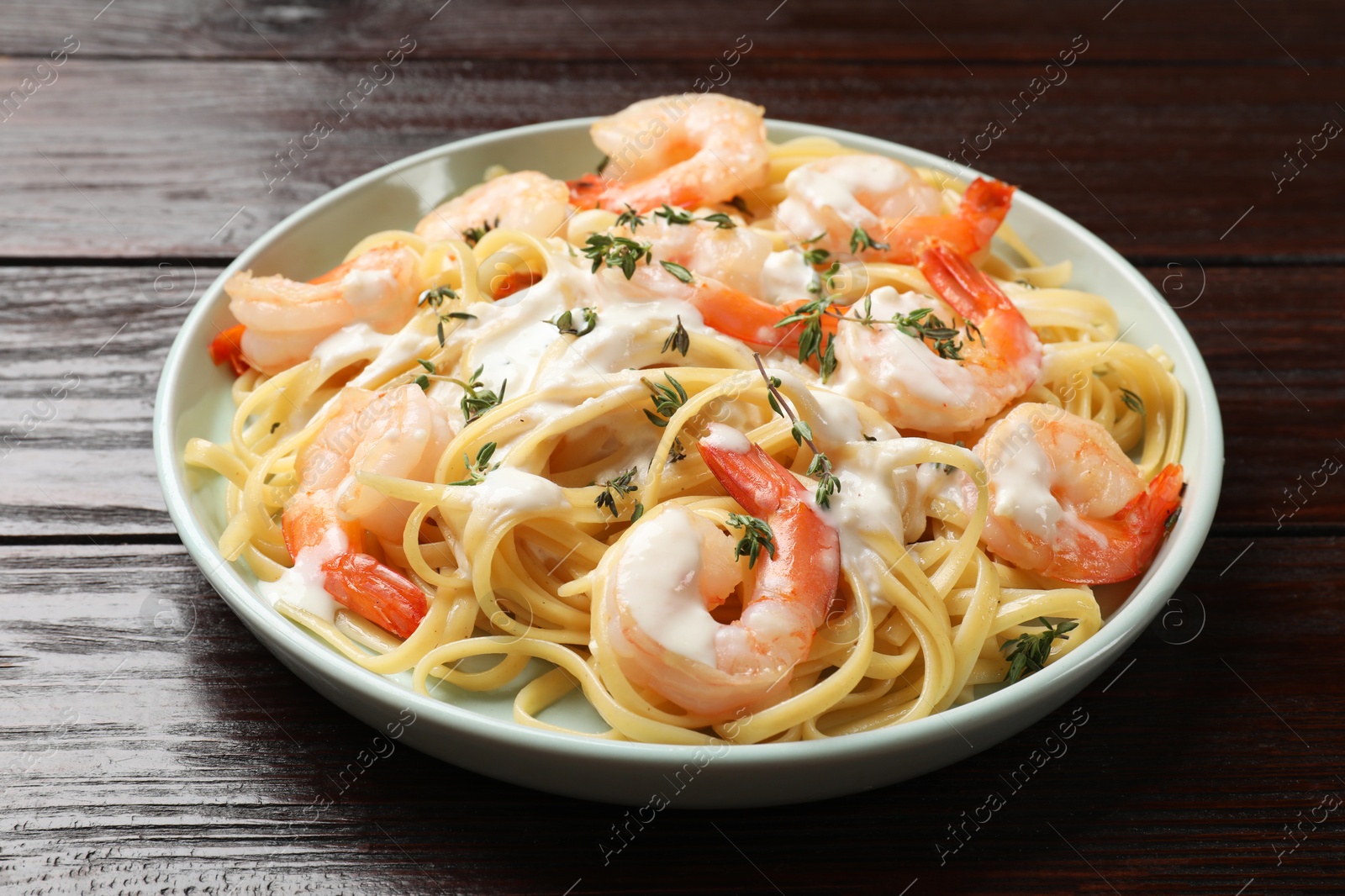 Photo of Delicious pasta with shrimps and creamy sauce on wooden table, closeup