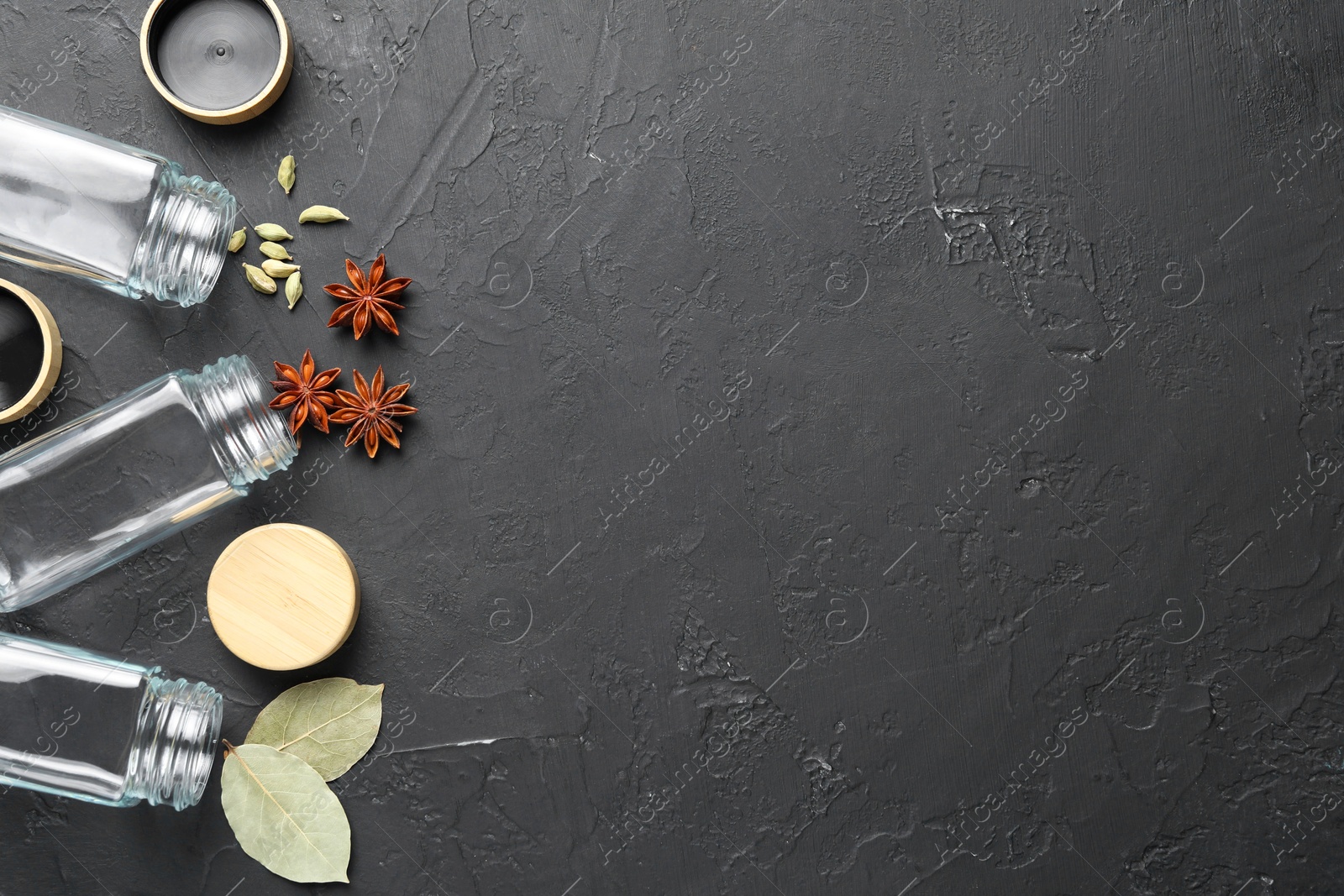 Photo of Different spices and glass jars on black table, flat lay. Space for text