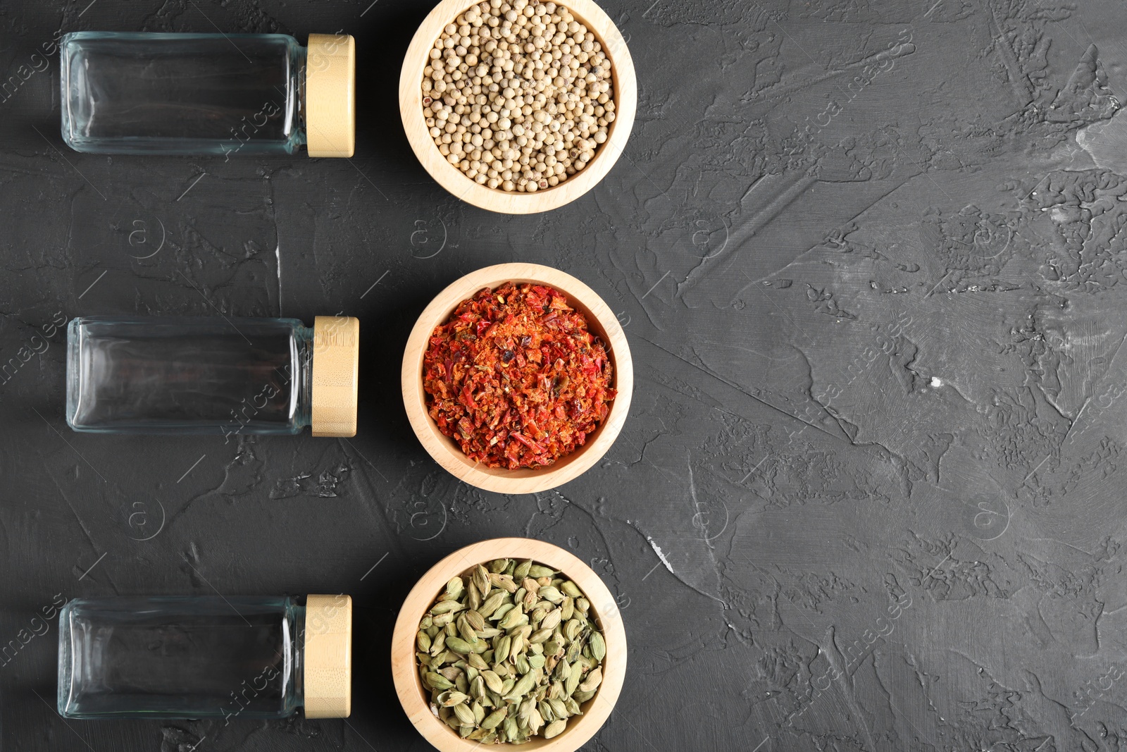 Photo of Different spices and glass jars on black table, flat lay. Space for text