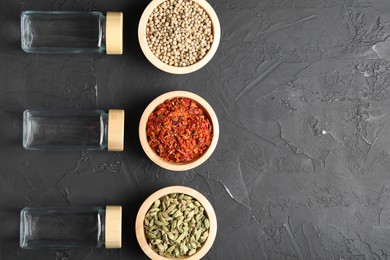 Different spices and glass jars on black table, flat lay. Space for text