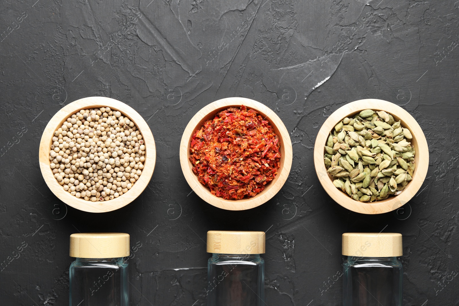 Photo of Different spices and glass jars on black table, flat lay