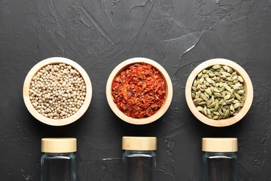 Photo of Different spices and glass jars on black table, flat lay