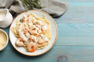 Tasty pasta with shrimps, creamy sauce and cheese on light blue wooden table, flat lay. Space for text