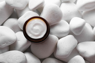 Face cream in jar on white stones, top view. Space for text