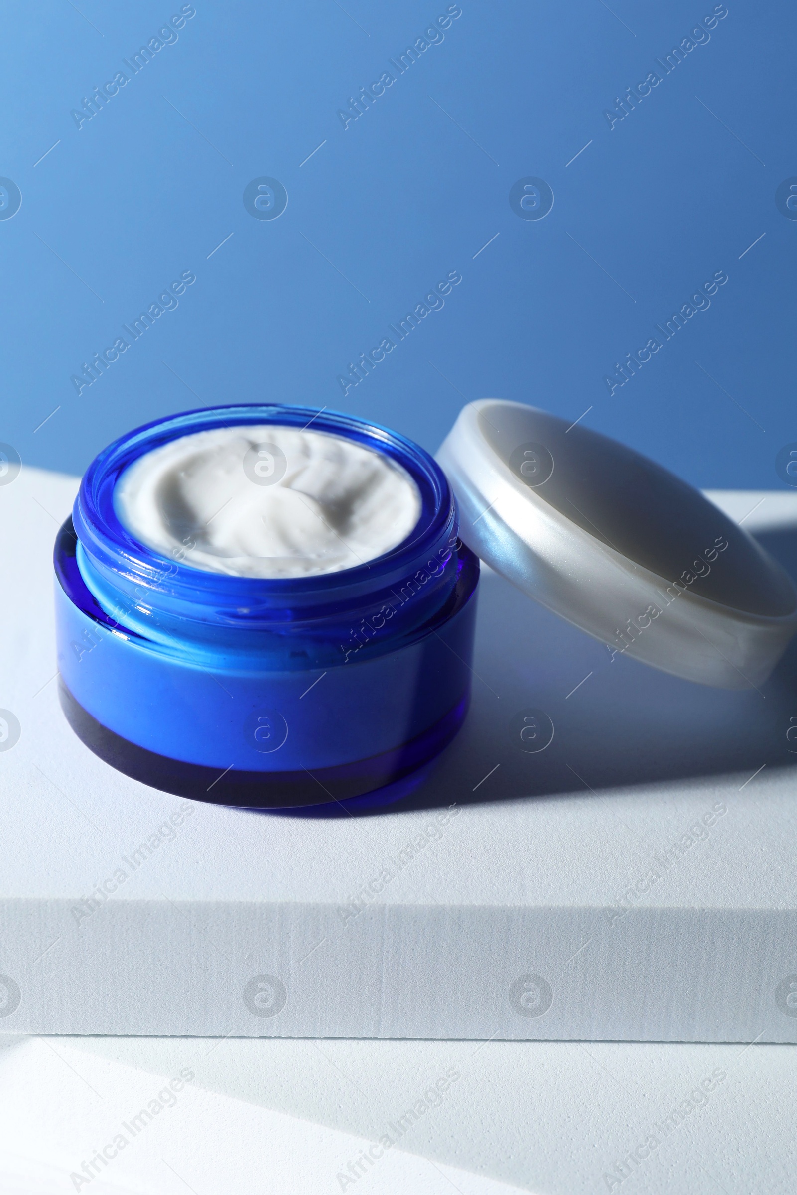 Photo of Stylish presentation of face cream in jar against light blue background