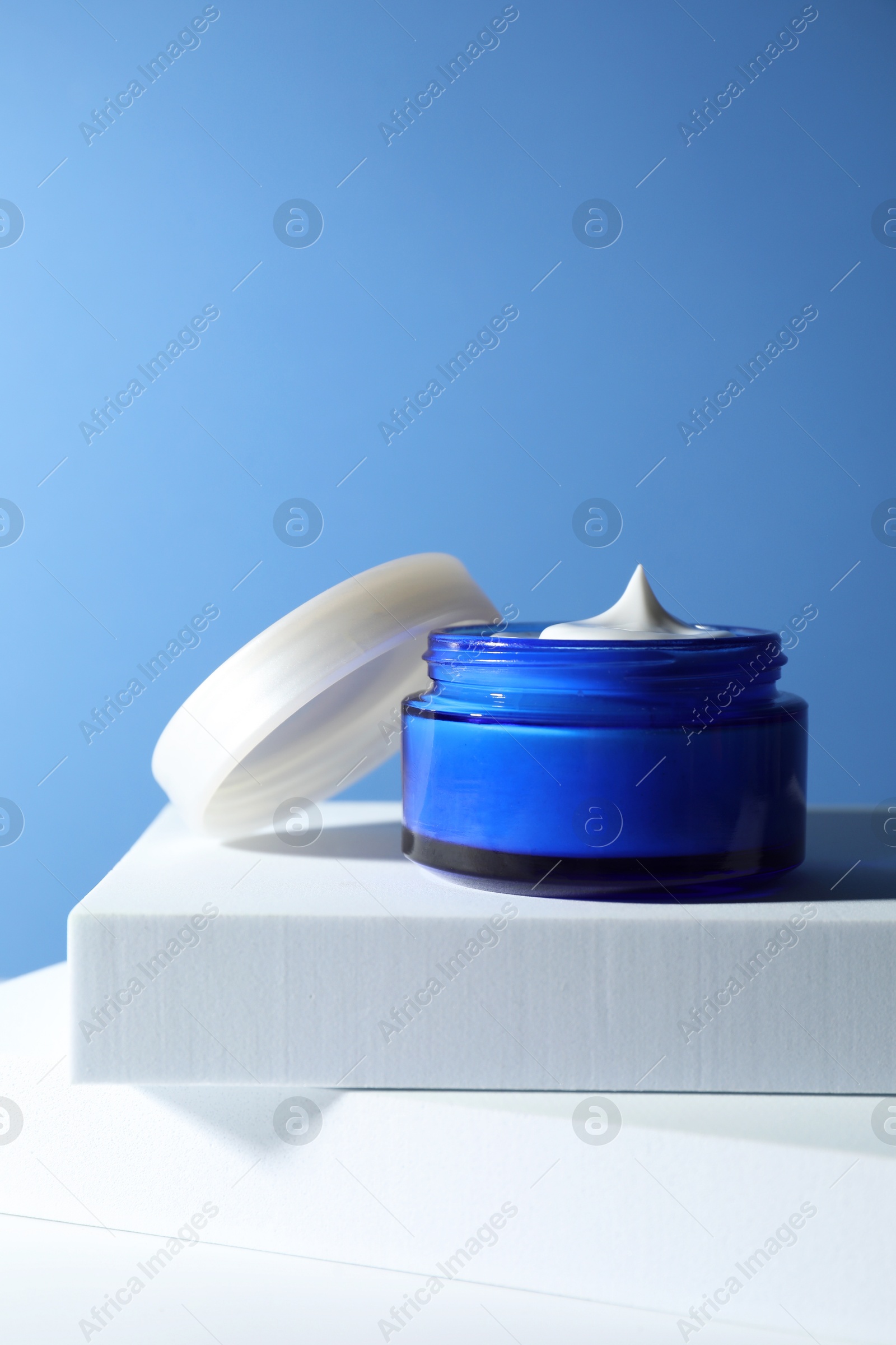 Photo of Stylish presentation of face cream in jar against light blue background