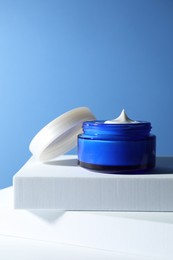 Photo of Stylish presentation of face cream in jar against light blue background