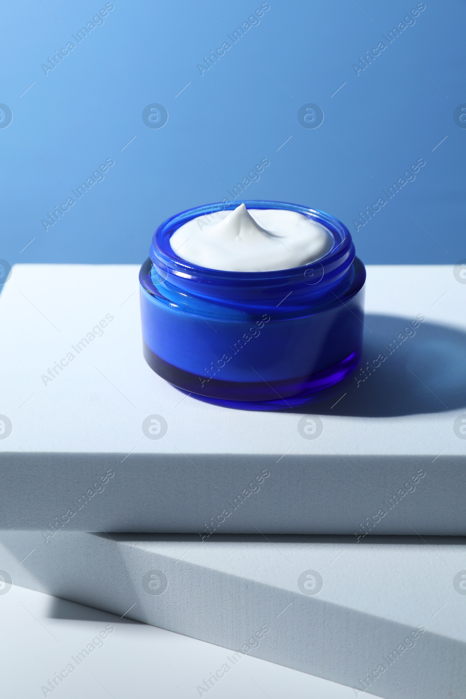 Photo of Stylish presentation of face cream in jar against light blue background