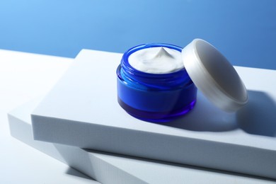 Photo of Stylish presentation of face cream in jar against light blue background