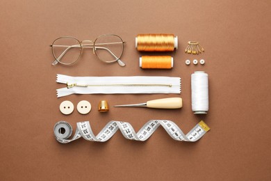 Photo of Flat lay composition with different sewing supplies and glasses on brown background