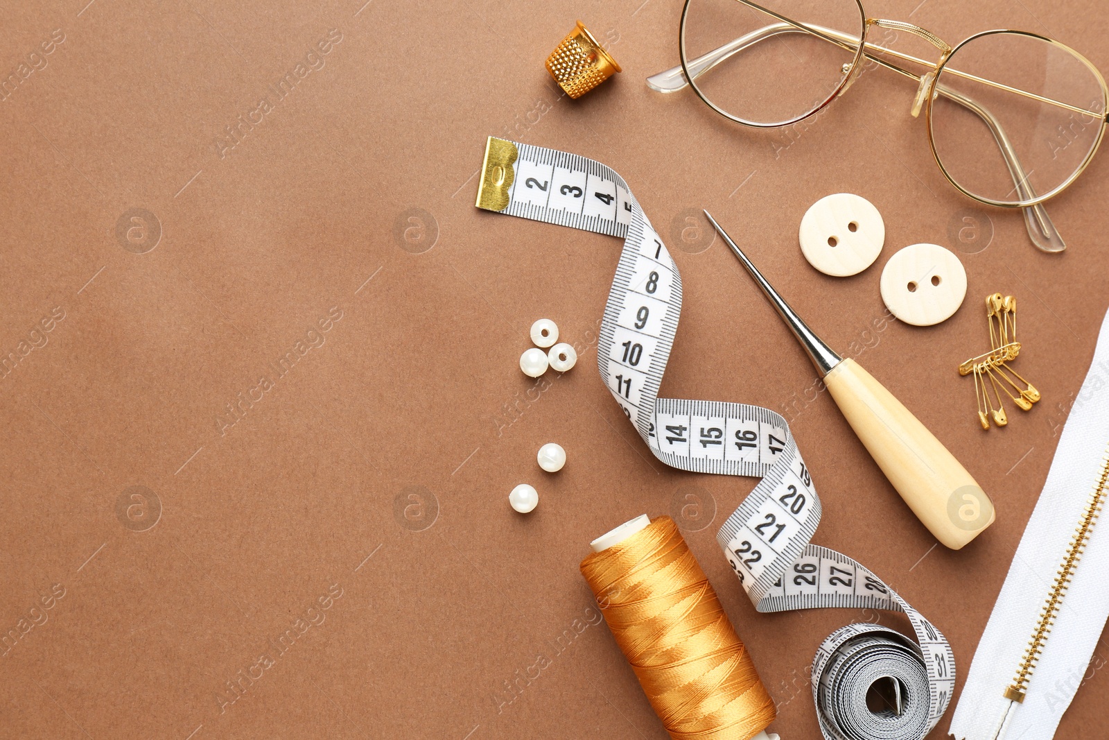 Photo of Flat lay composition with different sewing supplies and glasses on brown background. Space for text