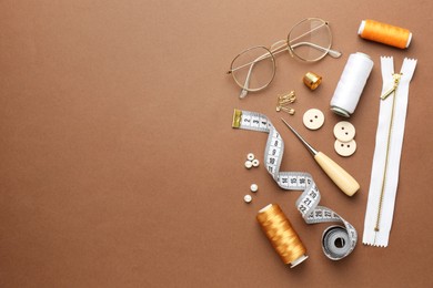 Flat lay composition with different sewing supplies and glasses on brown background. Space for text