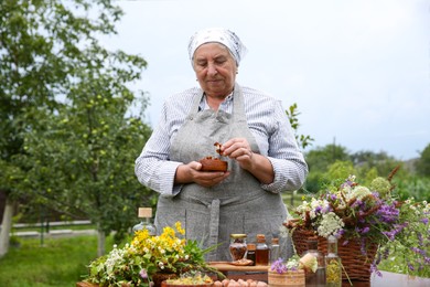 Senior woman with different ingredients for tincture at table outdoors