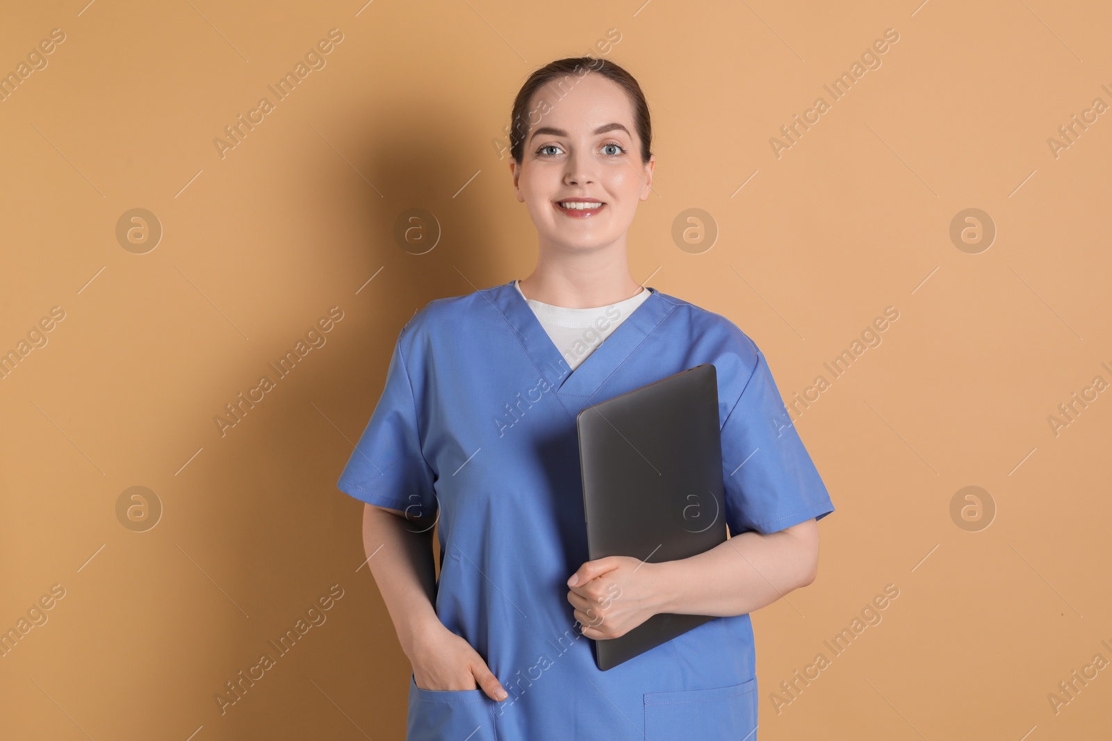 Photo of Portrait of nurse with laptop on dark beige background