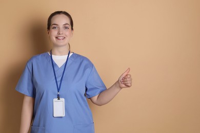 Photo of Professional nurse with badge showing thumbs up on dark beige background. Space for text