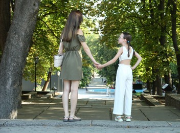 Mother and daughter holding hands in park, back view