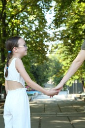 Photo of Little girl holding hands with mother in park, closeup