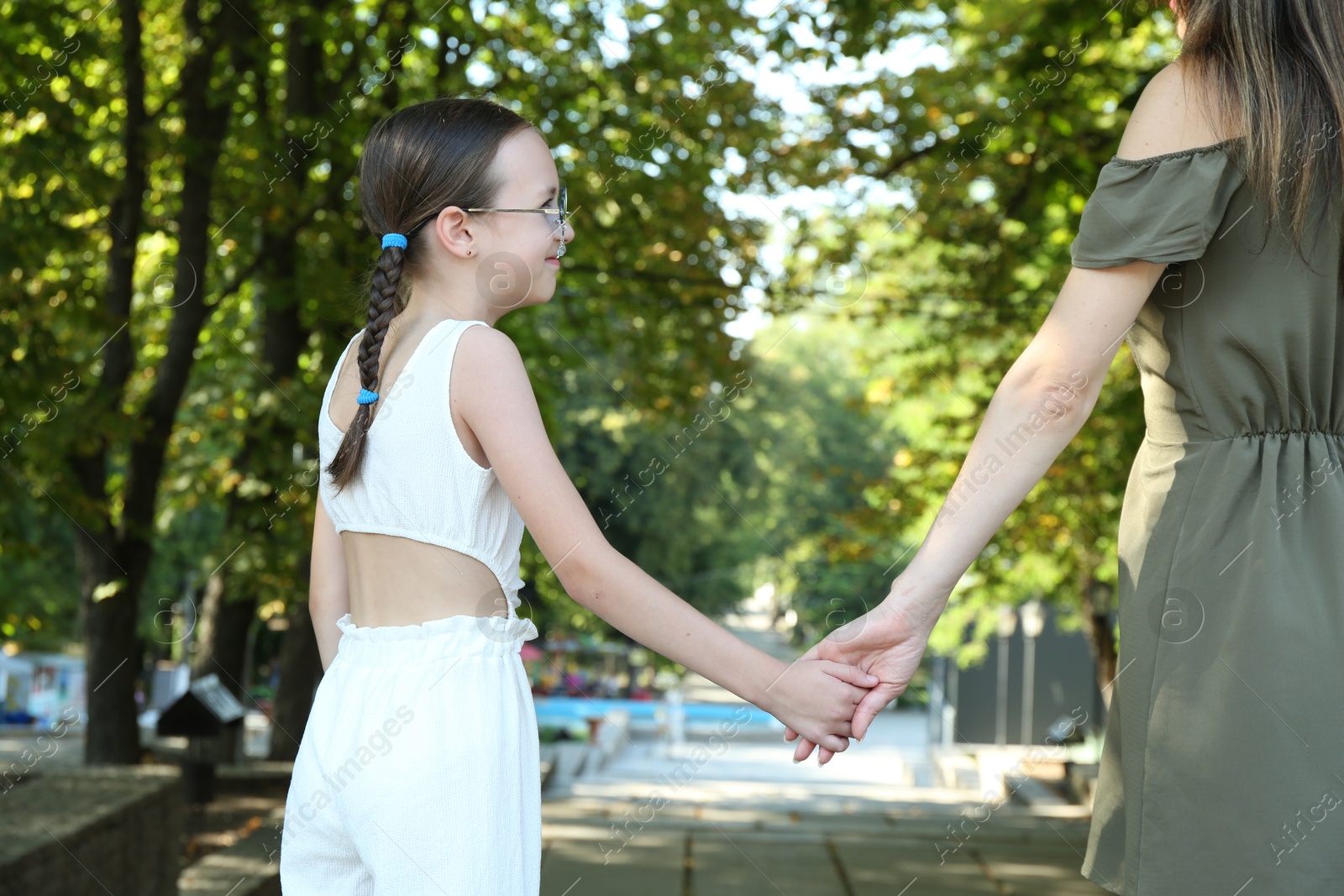 Photo of Little girl holding hands with mother in park, closeup