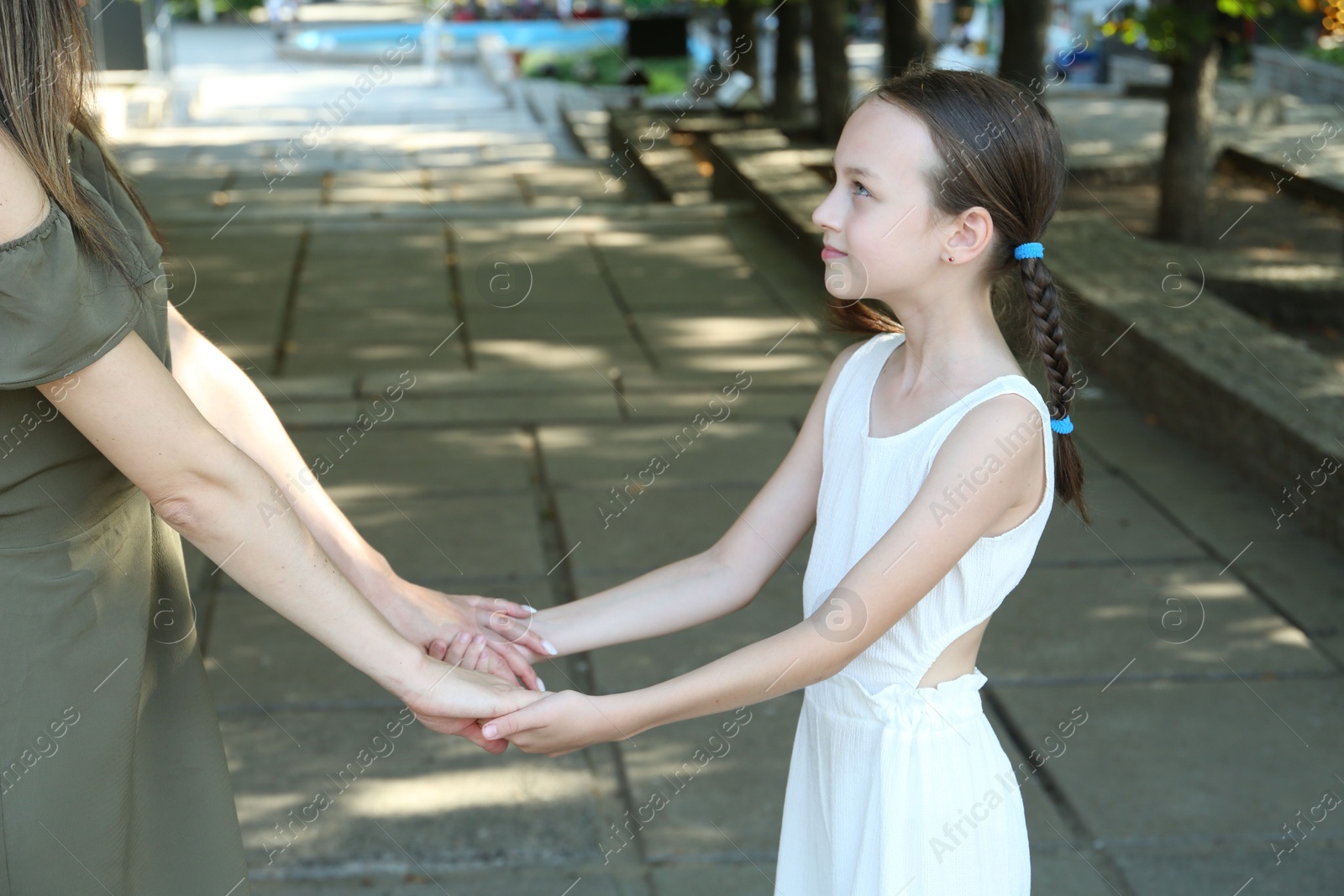 Photo of Little girl holding hands with mother in park, closeup