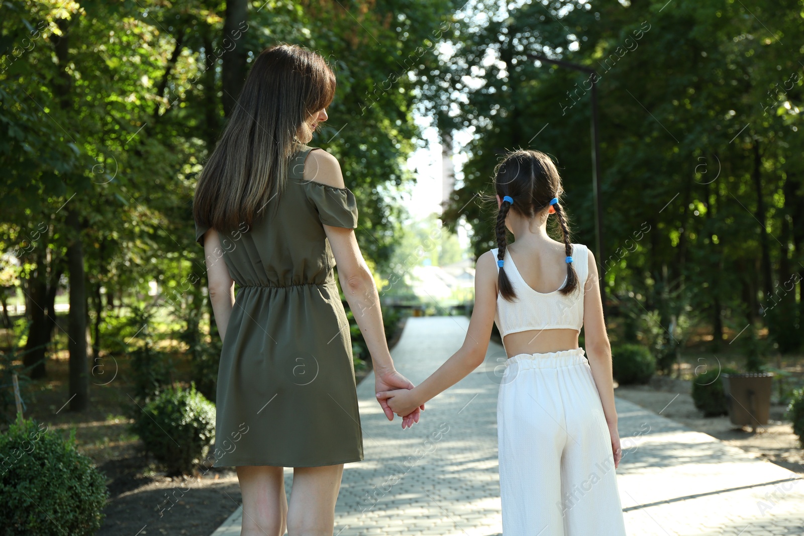 Photo of Mother and daughter holding hands in park, back view