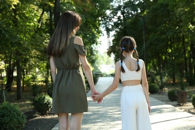 Photo of Mother and daughter holding hands in park, back view