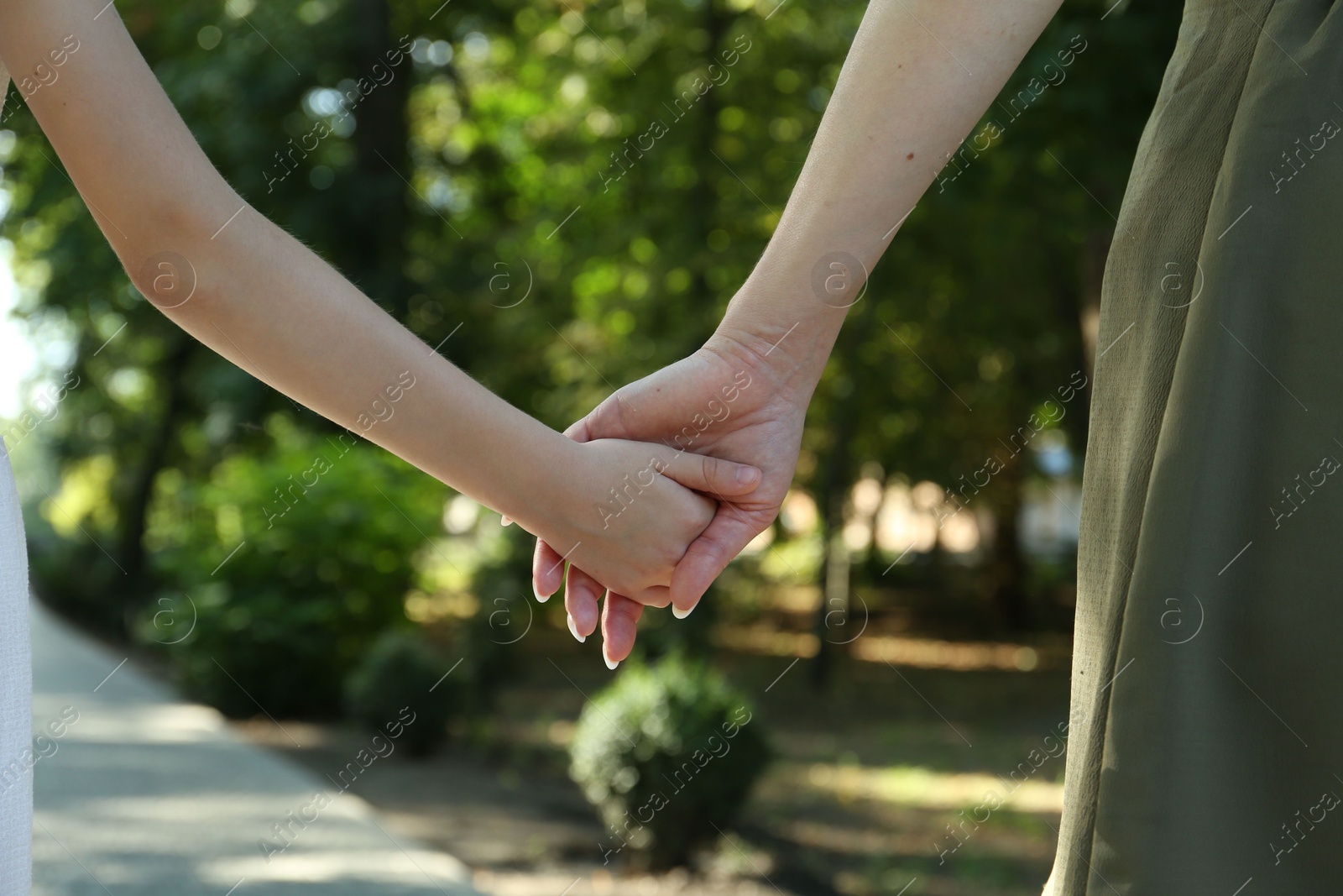 Photo of Mother and daughter holding hands in park, closeup