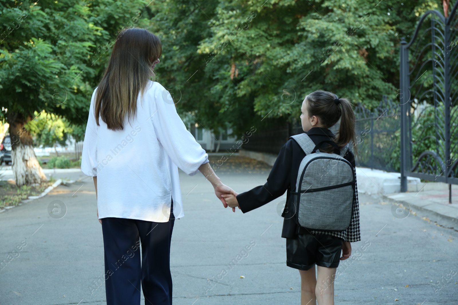 Photo of Mother and daughter holding hands outdoors, back view