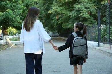 Mother and daughter holding hands outdoors, back view