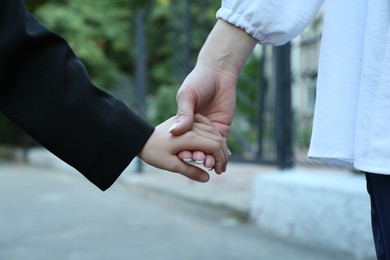 Photo of Mother and daughter holding hands outdoors, closeup