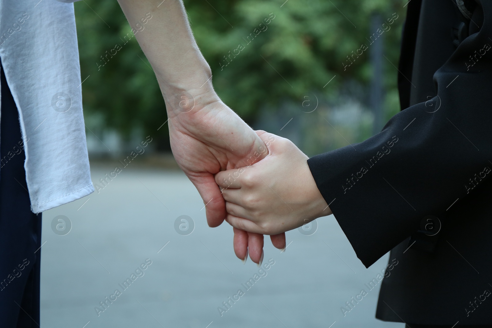 Photo of Mother and daughter holding hands outdoors, closeup