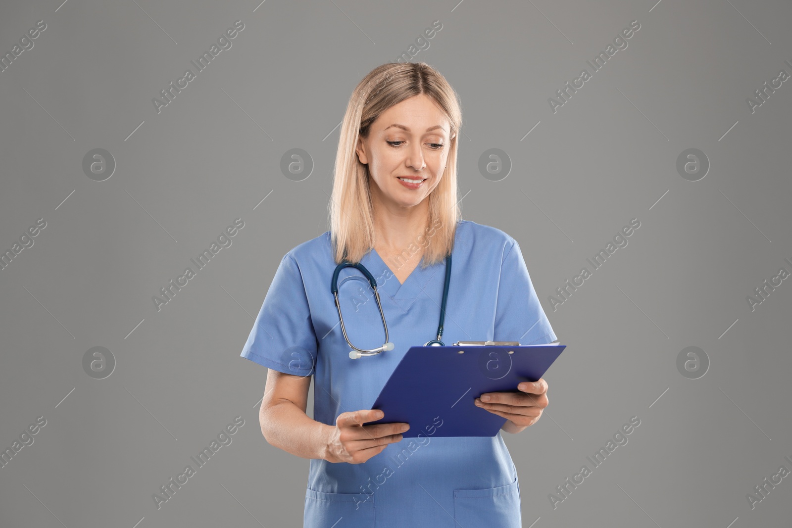 Photo of Nurse in medical uniform with stethoscope and clipboard on grey background