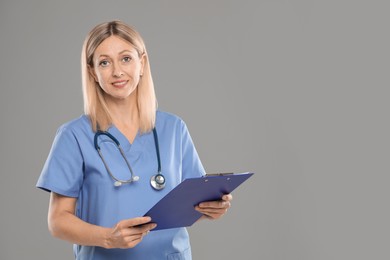 Portrait of nurse in medical uniform with stethoscope and clipboard on grey background, space for text