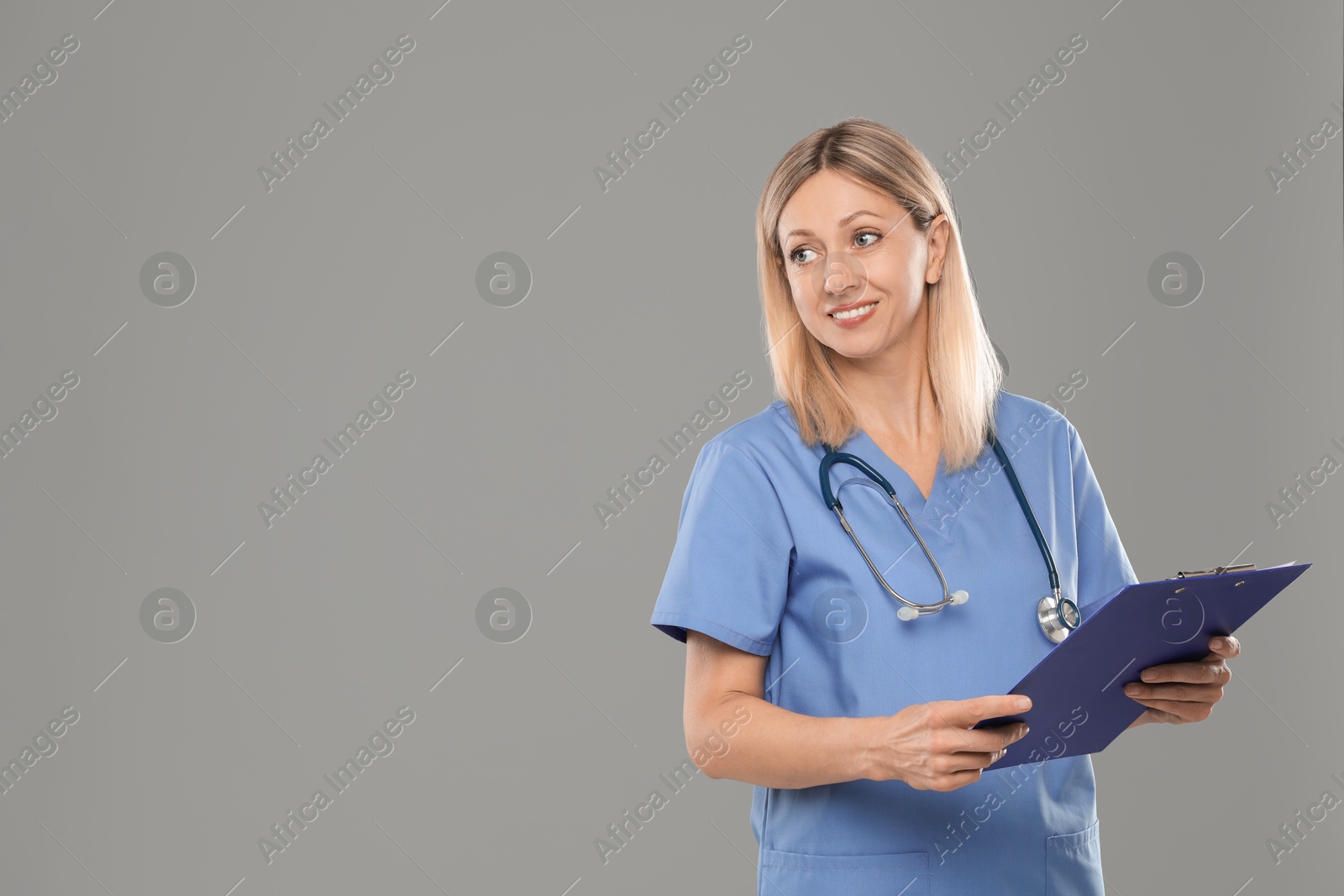 Photo of Portrait of nurse in medical uniform with stethoscope and clipboard on grey background, space for text