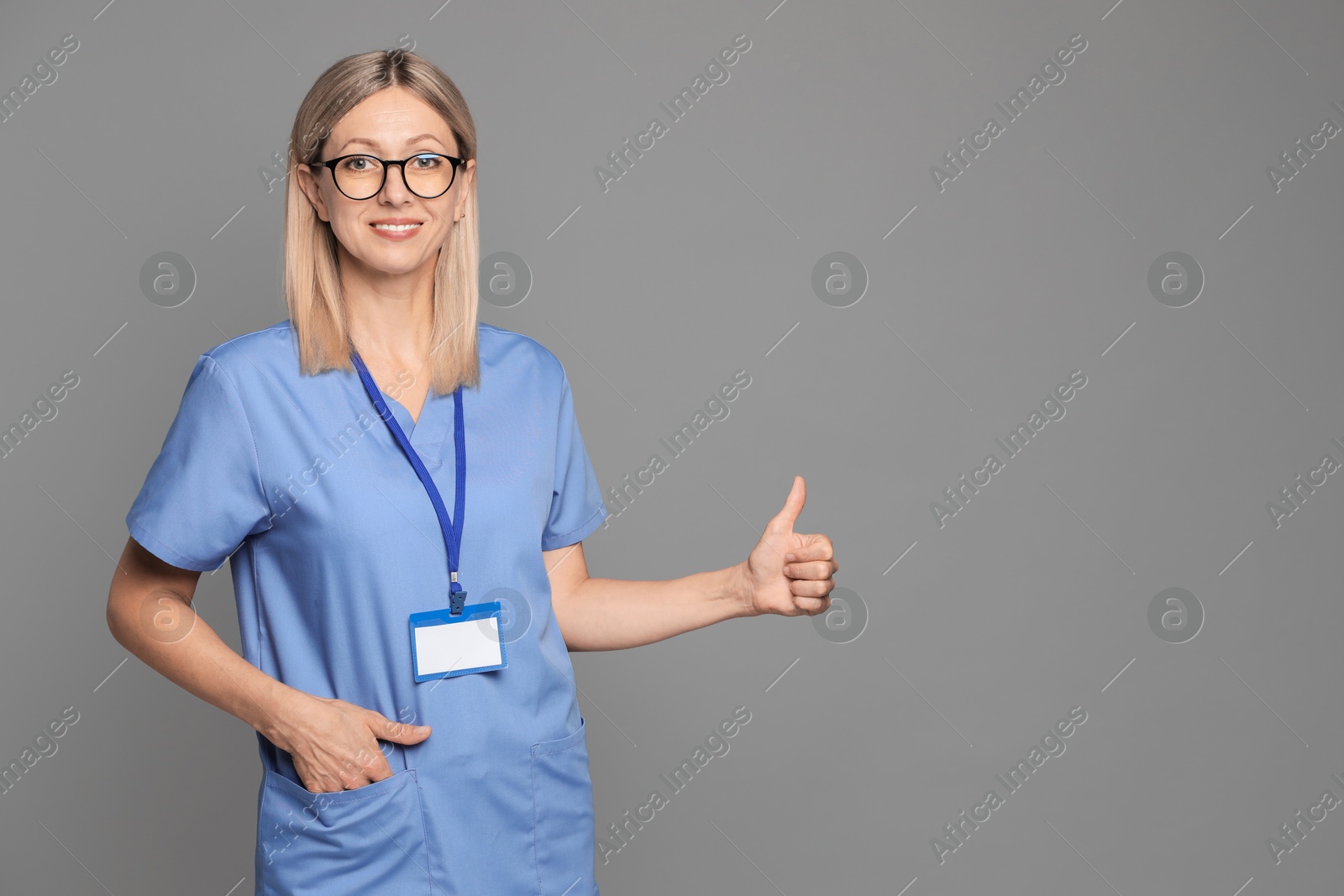 Photo of Nurse in medical uniform with badge showing thumbs up on grey background, space for text