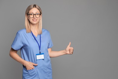 Photo of Nurse in medical uniform with badge showing thumbs up on grey background, space for text