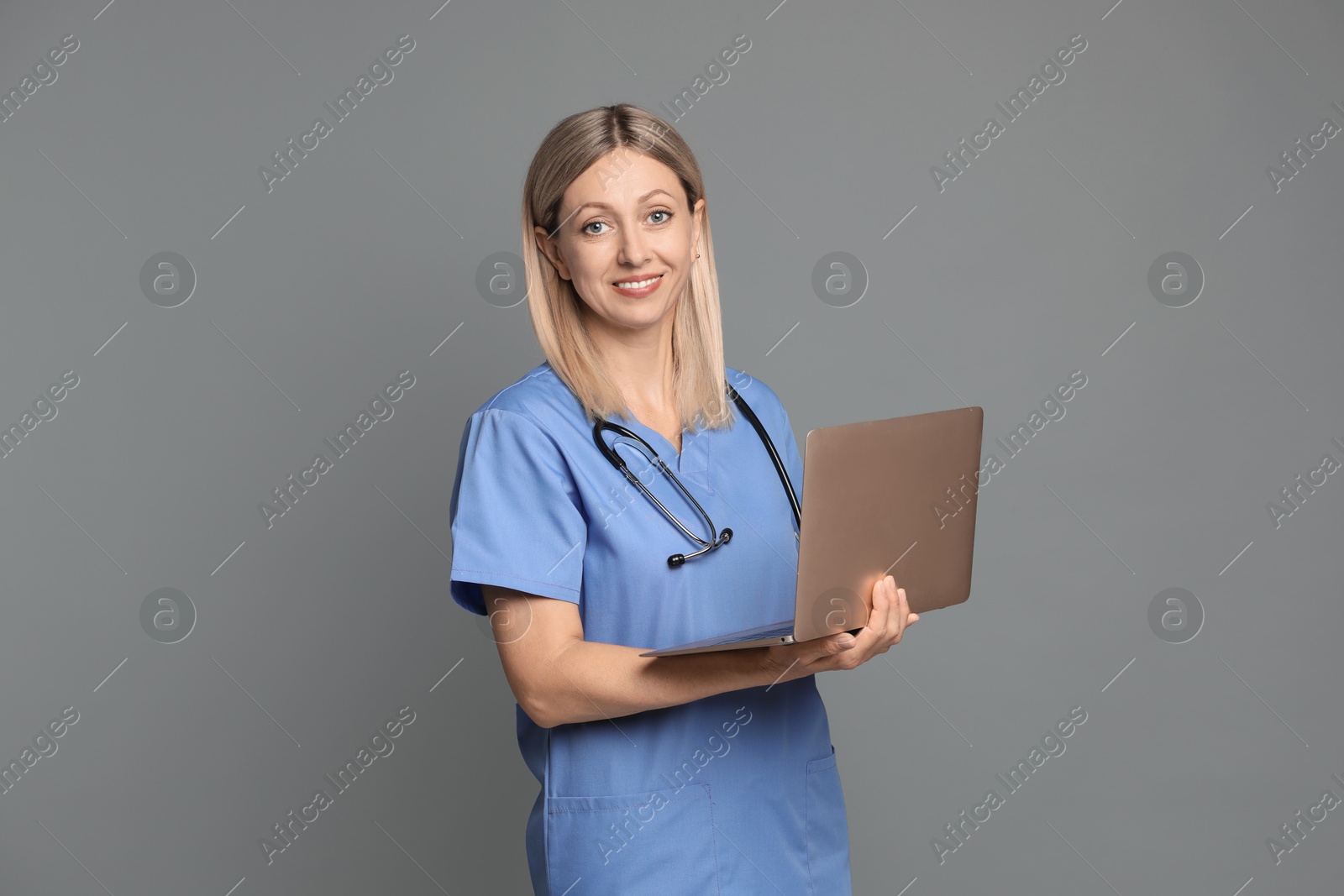 Photo of Doctor in medical uniform with stethoscope and laptop on grey background